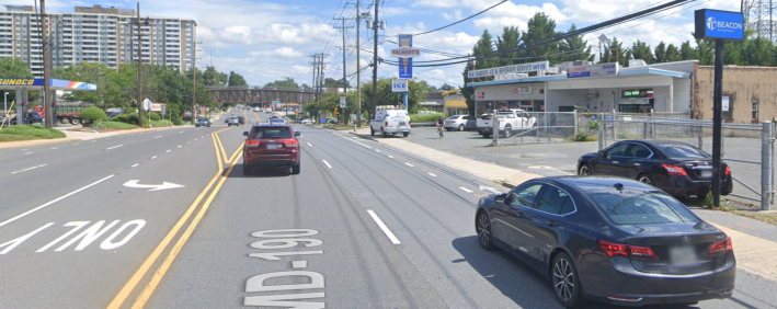Image description: The approximate site of the crash that killed Sarah Langenkamp, via Google Maps. Cars drive along a five-lane arterial; the painted bicycle lane where Langenkamp rode is obscured by the automobile to the right. In the image, a cyclist can be seen riding in a parking lot, and a large van is parked on the sidewalk.