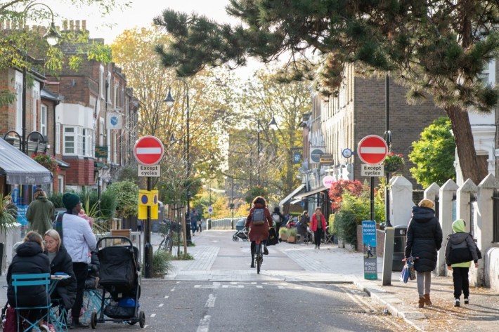 London has 85 low-traffic neighborhoods (LTN) that prioritize cycling and walking over driving. As shown in this photo, LTNs often feature narrowed roadways for motor vehicles, widened sidewalks for pedestrians and outdoor eating, prohibitions on through motor-vehicle traffic, reduced speed limits, and traffic-calming devices such as speed humps and raised crosswalks. Photo: Transport for London.
