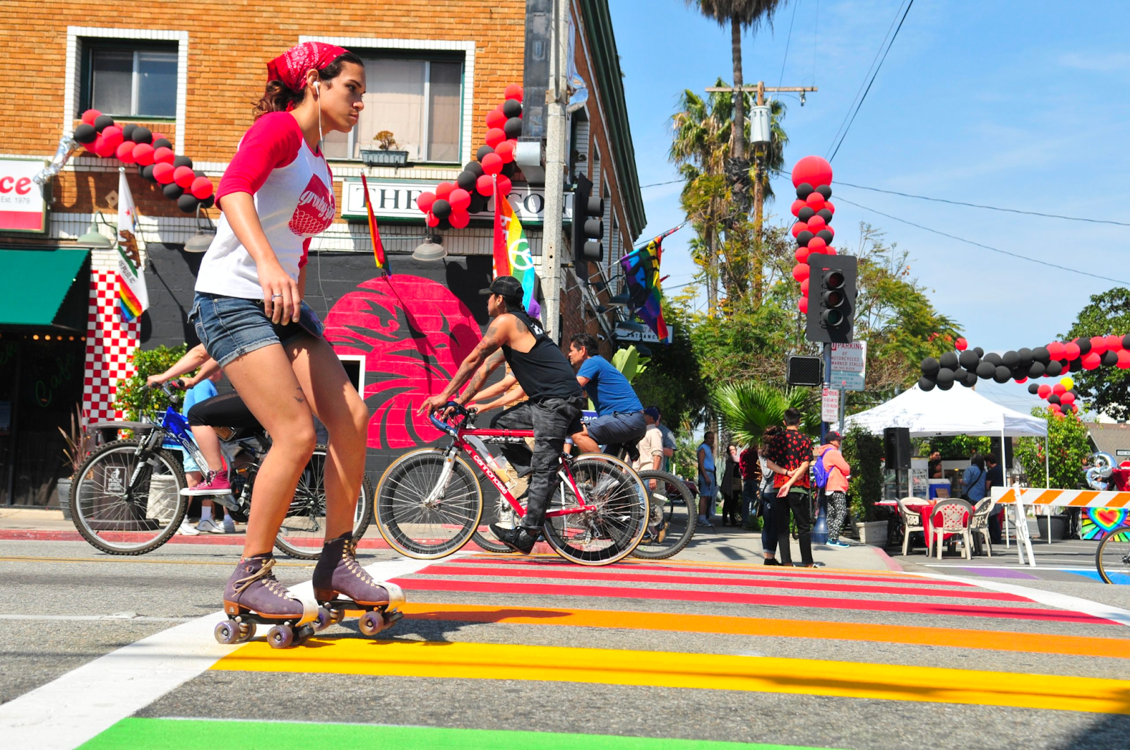 A roller skater and bicyclist cross a rainbow-colored crosswalk