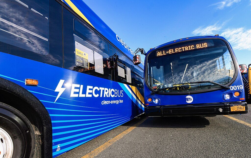 Two blue battery electric buses sit in a parking lot